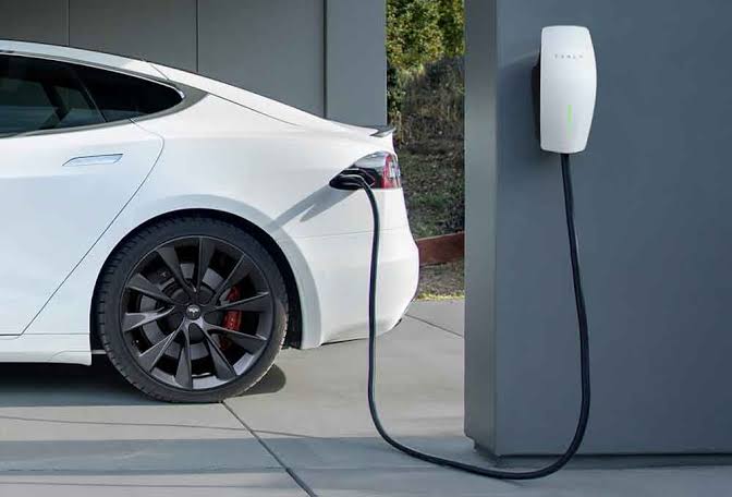 A white electric car charging from a wall-mounted charger